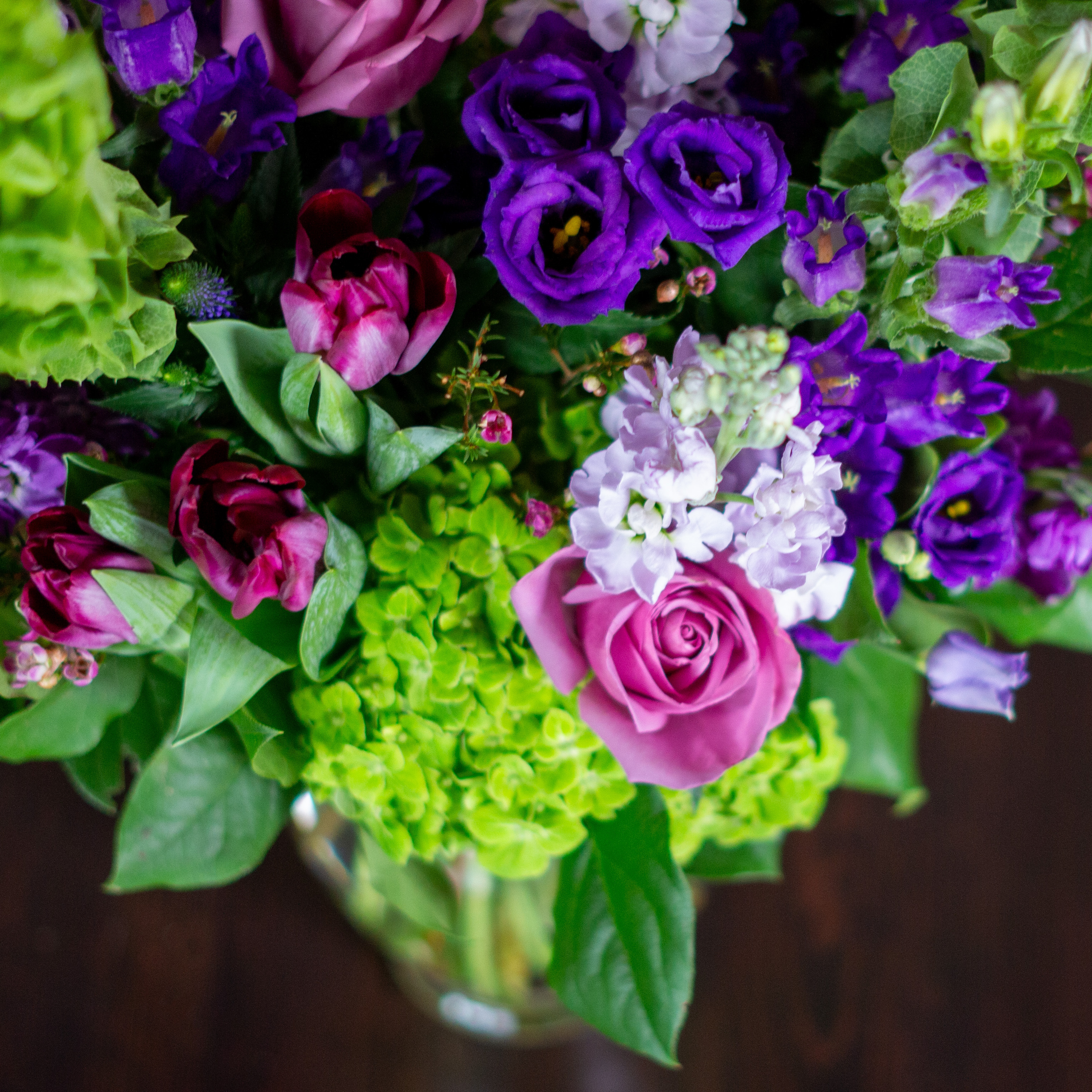 Peach valentines day flowers on a blue tablecloth. Flowers include peach roses, cream lisianthus, peach stock, white hydrangea, pink spray roses, and pink hypericum berries accented with eucalyptus. 