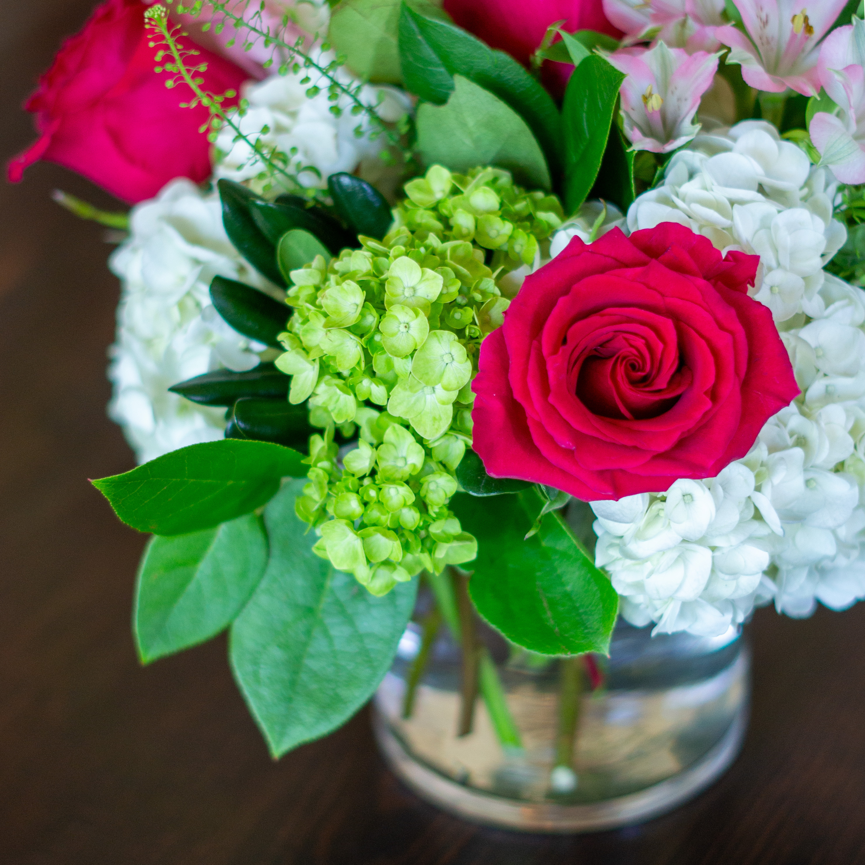 Peach valentines day flowers on a blue tablecloth. Flowers include peach roses, cream lisianthus, peach stock, white hydrangea, pink spray roses, and pink hypericum berries accented with eucalyptus. 