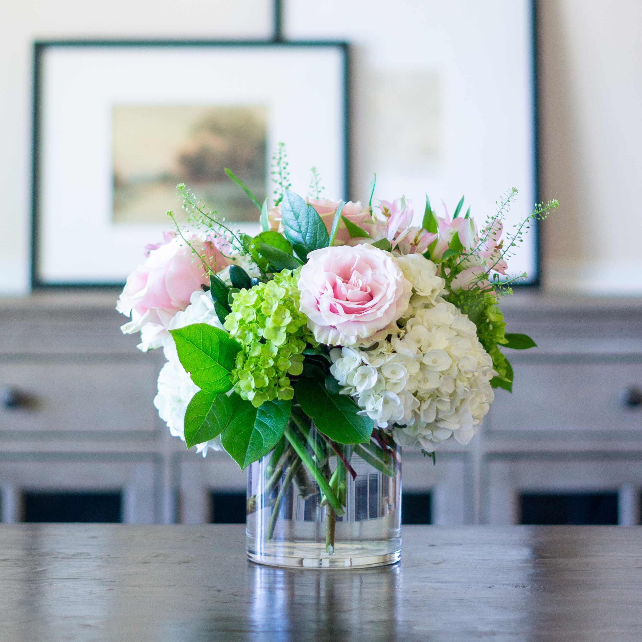 Peach valentines day flowers on a blue tablecloth. Flowers include peach roses, cream lisianthus, peach stock, white hydrangea, pink spray roses, and pink hypericum berries accented with eucalyptus. 