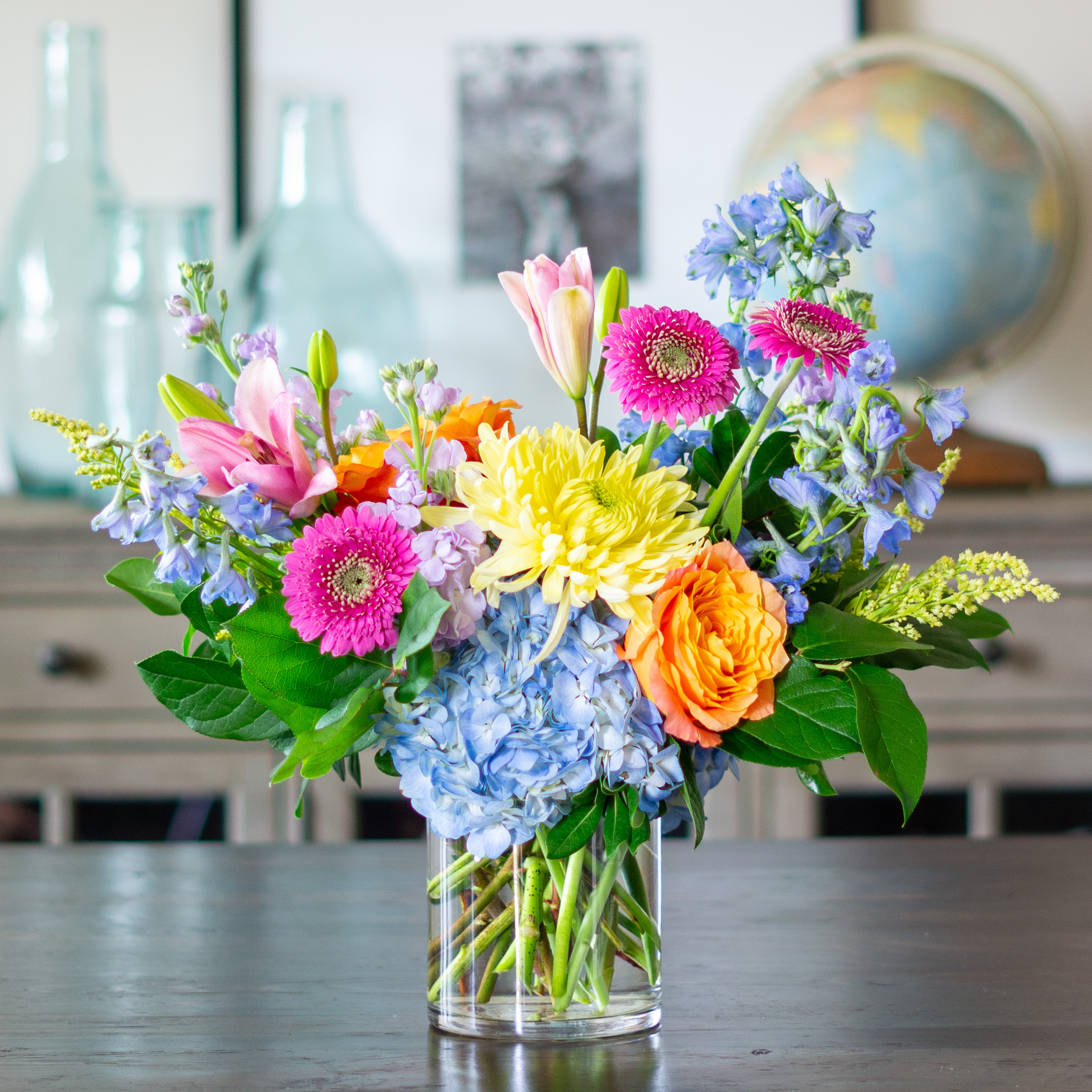 Peach valentines day flowers on a blue tablecloth. Flowers include peach roses, cream lisianthus, peach stock, white hydrangea, pink spray roses, and pink hypericum berries accented with eucalyptus. 