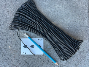 Bundle of black 275 nylon tactical cord on concrete with a pencil and playing card for size reference showing length and thickness.