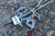 Gravity XL grappling hook components on rocky ground with cross piece and main body, shown with a playing card, quarter, and pencil for size reference.