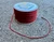 Spool of red and black Razorback micro 90 nylon paracord on concrete with loose end extended, showing thin diameter and length.