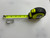 Small MicroFin carabiner placed next to an extended tape measure on a white textured surface, showing its length for size reference.
