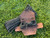 Brown leather Firecracker paracord dispenser opened on grass with black paracord partially wrapped inside and a larger coil of paracord placed behind it.