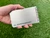 Hand holding a small spiral notebook with a brushed titanium cover labeled “M. Derreberry” against a grass background.