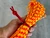 Hand holding a bundle of orange and yellow paracord secured with a red cord threaded through a leather toggle slide.