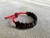 Black paracord bracelet with a red adjustable cord secured using a leather toggle slide on a textured surface.