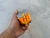 Hand holding a compact bolt-style spool wrapped with orange and yellow paracord.