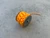 Compact metal bolt-style spool wrapped with orange and yellow paracord, resting on a concrete surface.