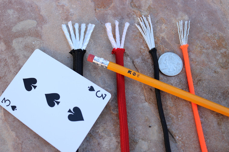 Multiple strands of paracord in different colors displayed together next to a playing card, a pencil and a quarter to show sizing.
