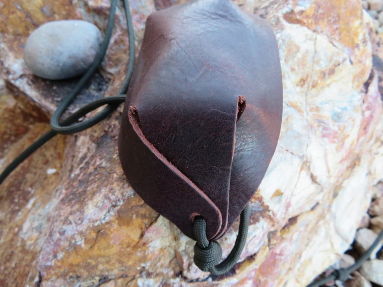 Leather sling pouch fully assembled with paracord cords attached on both sides for use.