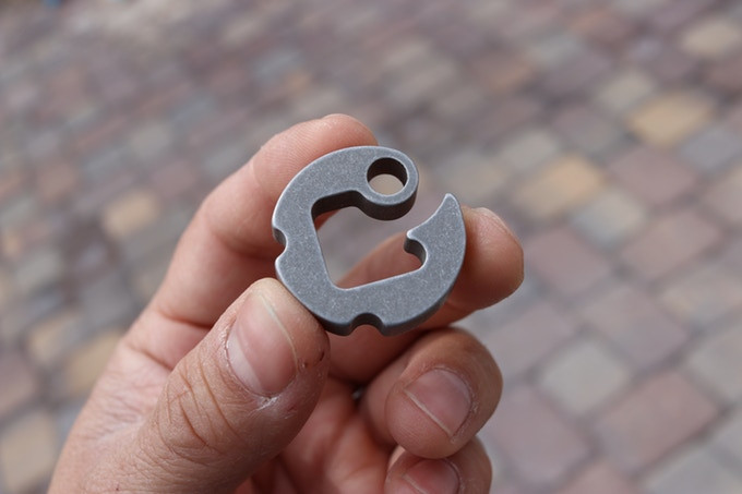 Blackwall paracord hook held in hand showing compact aluminum design with cord slot and attachment hole.