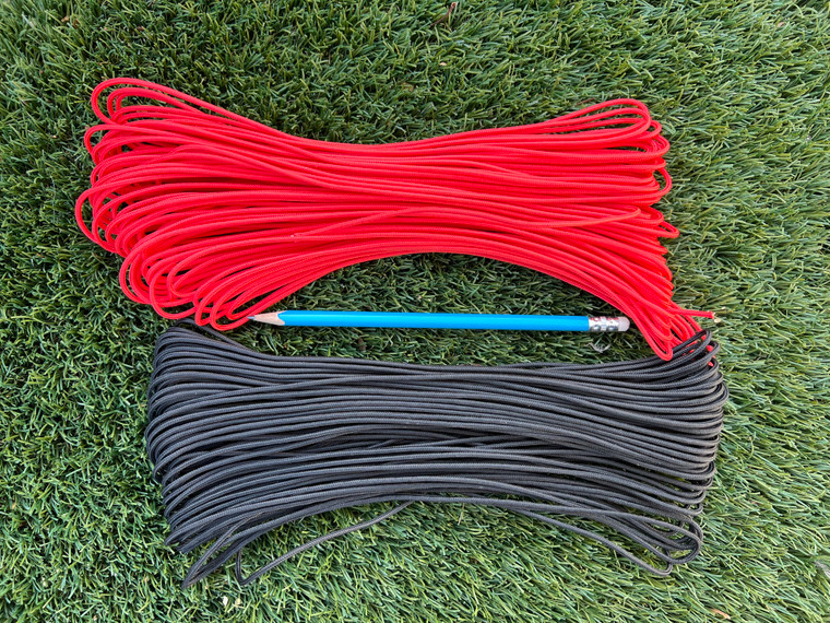 Red and black 275 nylon tactical cord bundles laid out on grass with a pencil for size reference showing 100-foot lengths.