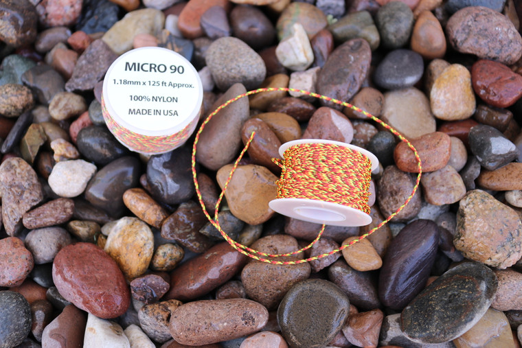 Spool of micro 90 nylon paracord resting on small rocks, showing compact size and thin cord profile.