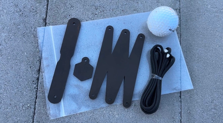 Leather Mini Sling pieces laid out on a plastic bag, next to a black paracord bundle and a golf ball.