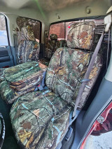 Front cabin of a truck showing custom Realtree Camo seat covers on the bucket seats and center console, providing heavy-duty protection against spills and wear.