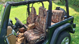 Realtree waterproof camo seat covers in a Jeep with front and rear seats covered, matching wheel cover on grass.