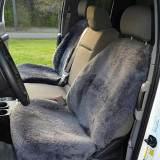 Front bucket seats of a white truck outfitted with dark charcoal grey sheepskin seat covers, offering a soft, high-pile texture for enhanced comfort during long drives.