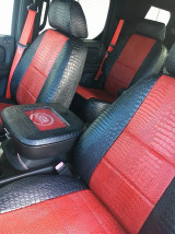 Front bucket seats in a Cadillac featuring black and red exotic seat covers with a textured crocodile finish, complemented by a matching custom center console cover for a high-end, personalized look.