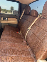 A rear bench seat in a truck outfitted with brown exotic seat covers, showcasing a detailed crocodile skin pattern that adds a rugged yet sophisticated touch to the interior.