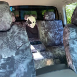 Comprehensive interior view showing rear bench and front seat backs fully outfitted with dark Kryptek® Camo covers, including a functional center armrest and cupholder cutout.