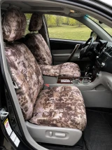 Front interior of a vehicle featuring custom-fit Kryptek® "Highlander" camo seat covers on the bucket seats and center console, providing a rugged, desert-inspired aesthetic.