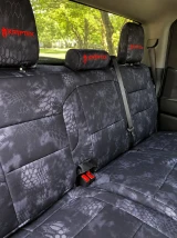 Rear bench seat of a truck outfitted with Kryptek® "Typhon" camo seat covers, featuring a dark tactical scale pattern and custom red embroidered headrest logos.