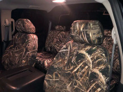 Full interior view of a vehicle at night, showing both front and rear seats completely protected by durable Realtree Camo seat covers.