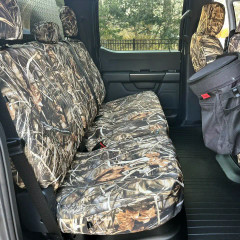 Rear bench seat of a truck fully protected by Realtree Camo seat covers, featuring a realistic marshland pattern and a convenient hanging storage organizer.