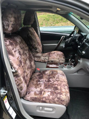 Front interior of a vehicle featuring custom-fit Kryptek® "Highlander" camo seat covers on the bucket seats and center console, providing a rugged, desert-inspired aesthetic.