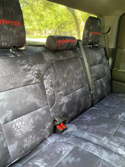Rear bench seat of a truck outfitted with Kryptek® "Typhon" camo seat covers, featuring a dark tactical scale pattern and custom red embroidered headrest logos.