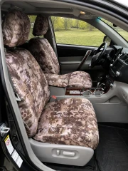 Front interior of a vehicle featuring custom-fit Kryptek® "Highlander" camo seat covers on the bucket seats and center console, providing a rugged, desert-inspired aesthetic.