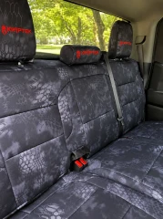 Rear bench seat of a truck outfitted with Kryptek® "Typhon" camo seat covers, featuring a dark tactical scale pattern and custom red embroidered headrest logos.