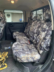 Rear bench seat of a pickup truck fully outfitted with custom Kryptek® Waterproof Camo seat covers in the earthy "Highlander" pattern.