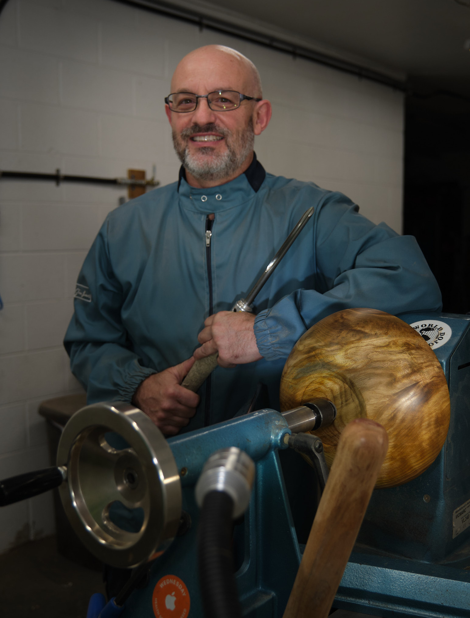 Zvi, owner of ZK Creations, standing in front of his lathe holding a woodturning tool in his workshop in Prescott, Arizona.