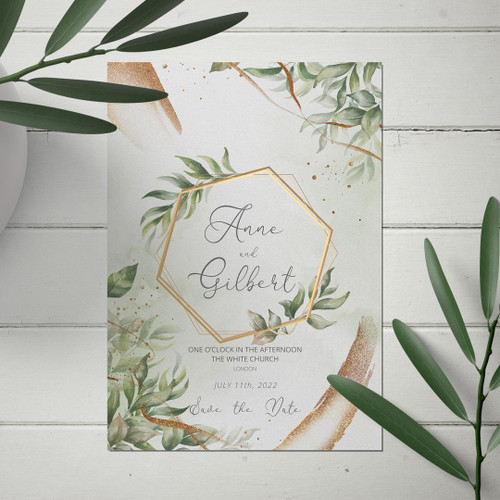 Embellished Wedding Invites, elegant wedding invitation card with green foliage and gold accents on a white wooden background.