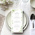 Wedding Menus, elegant white wedding dinner menu card with green leaf design on a table setting with plates, glasses, and cutlery.