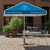 Square Parasols, outdoor patio setup with a blue square parasol providing shade over a white metal table and chairs on a cobblestone surface.