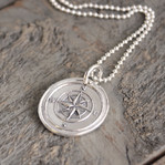 Compass Wax Seal Inspired Necklace on a sterling ball chain laying on a rough piece of wood