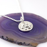 1/2" round silver paw print with a heart in the center on a silver bead style chain, laying on a polished purple agate slice, looking from slight left front side