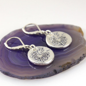 Dandelion Token Charm Earrings laying on a purple geode slice