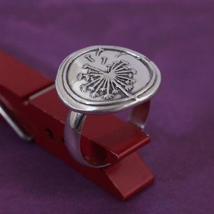 Dandelion Wax Seal Inspired Ring held up with a red clothes pin on a purple background