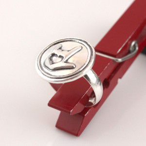 ASL I Love You Symbol Wax Seal Inspired Ring held up in a red clothespin on a white background