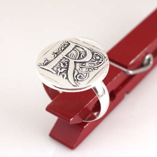 Initial Cap Wax Seal Inspired Ring held up in a red clothespin on a white background from another angle