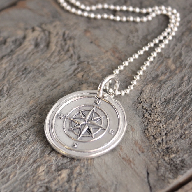 Compass Wax Seal Inspired Necklace on a sterling ball chain laying on a rough piece of wood