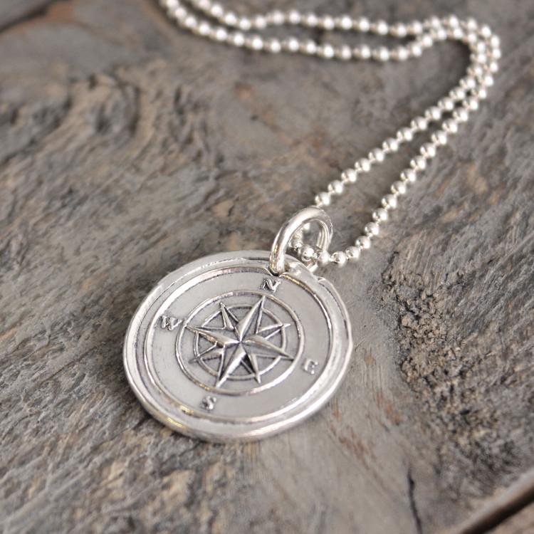 Compass Wax Seal Inspired Necklace on a sterling ball chain laying on a rough piece of wood