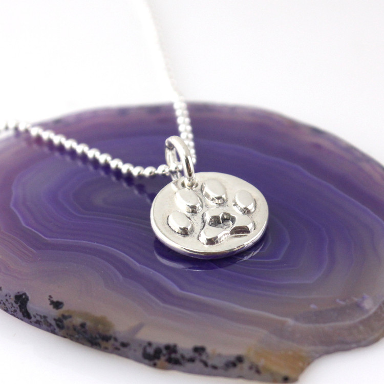 1/2" round silver paw print with a heart in the center on a silver bead style chain, laying on a polished purple agate slice, looking from slight left front side - ready to ship