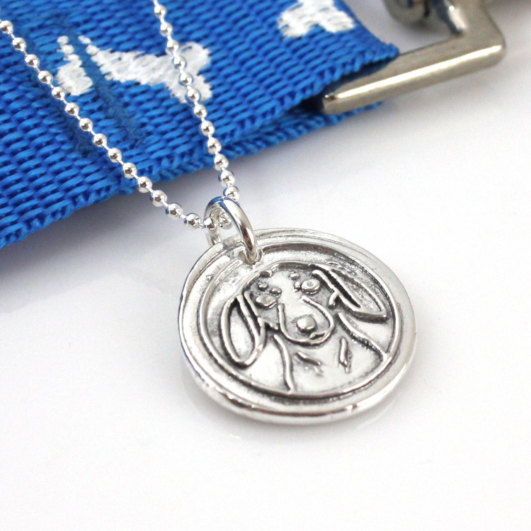 Dachshund Wax Seal Inspired Necklace laying next to a blue leash with white bones on it