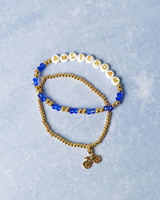 Set elastische kralen armbandjes van Heinen Delfts Blauw. Eén met goudkleurige kraaltjes en een bedeltje van een fiets. De ander met kralen die het woord Amsterdam spellen. Set elastische kralen armbandjes van Heinen Delfts Blauw. Eén met goudkleurige kraaltjes en een bedeltje van een fiets. De ander met kralen die het woord Amsterdam spellen.